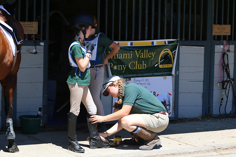 Stable manager assisting a younger rider by polishing her boots before she rides.