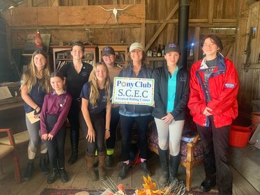 A group of girls and young women holding a Pony Club sign, smiling at the camera.