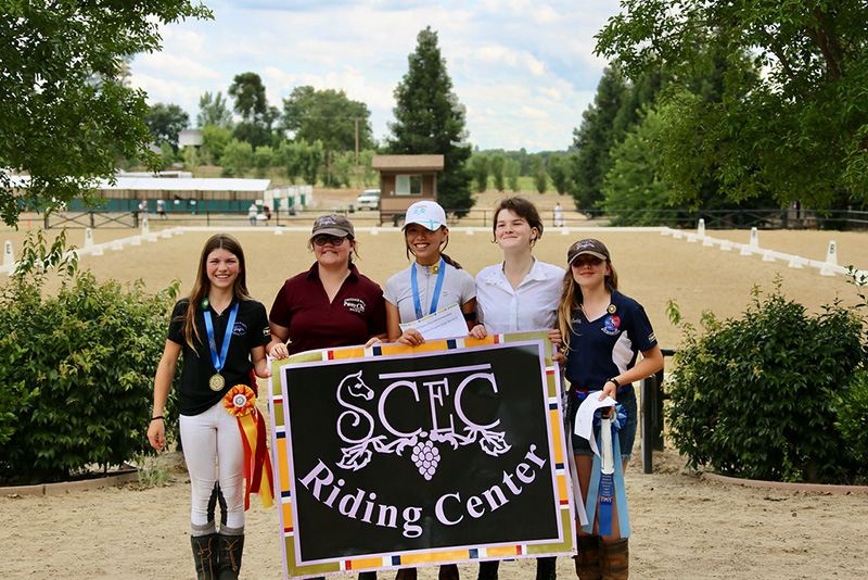 Five girls holding a sign standing in front of the camera, smiling.