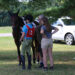 A group of three people standing at a horse, one is pointing out something on the horse's tack.