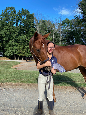 A young girl standing next to her horse, smiling at the camera.