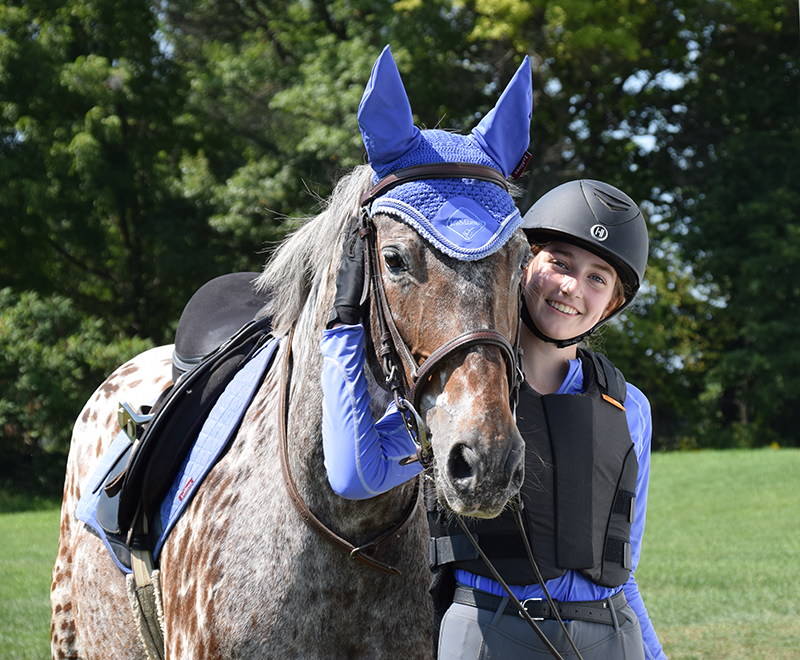 A girl hugging her horse beside a trailer, smiling at the camera.