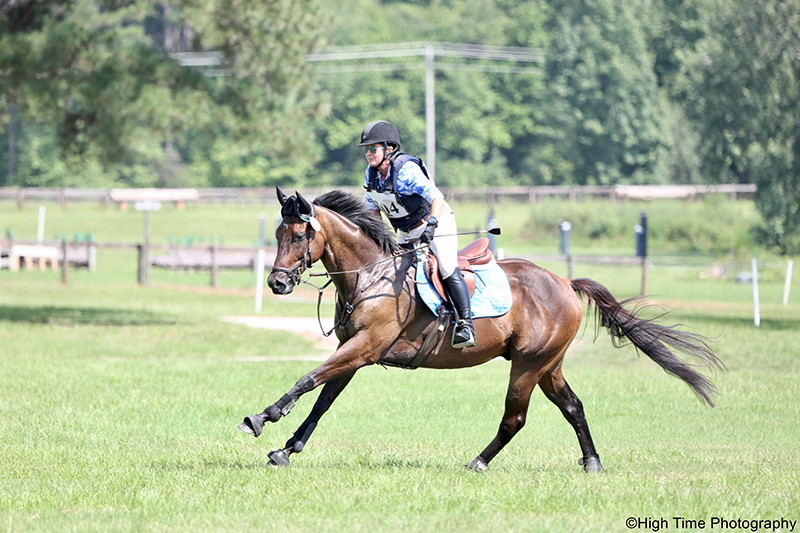 A woman riding her horse outside on a cross-country course.