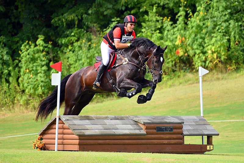 A man jumping his horse outside over a jump on a cross-country course.