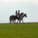 Two young riders on horses hacking across a hill.