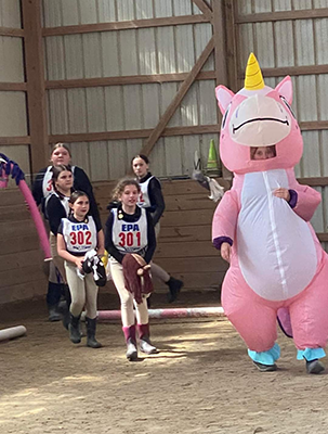A group of young kids with stick horses and one in an inflatable unicorn costume.
