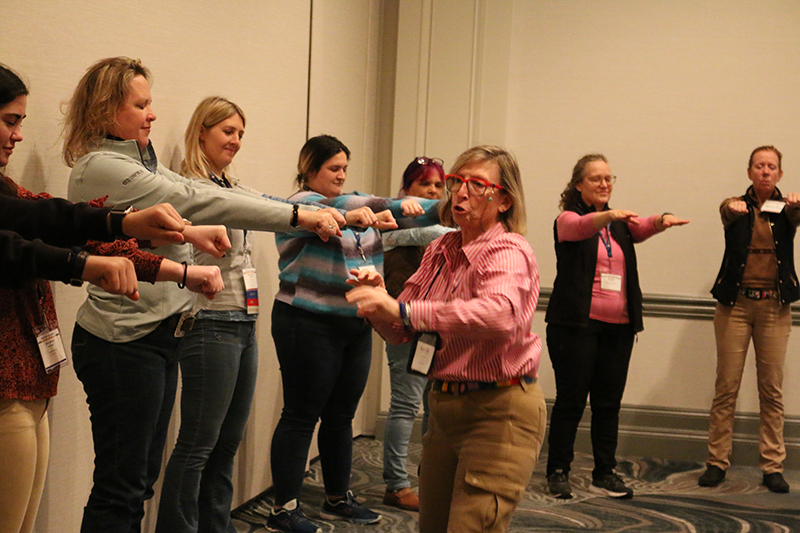 A woman demonstrating a hand movement to other individuals in line in front of her.  