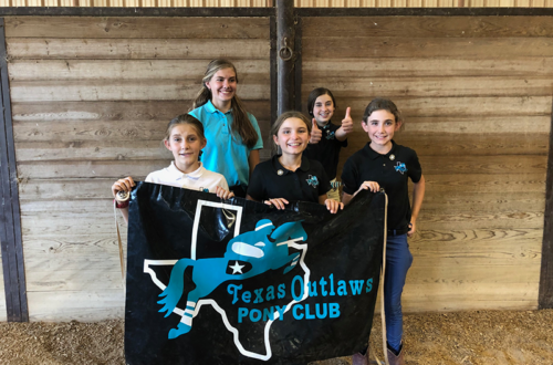 A group of young girls holding a banner with the name of their Pony Club on it.