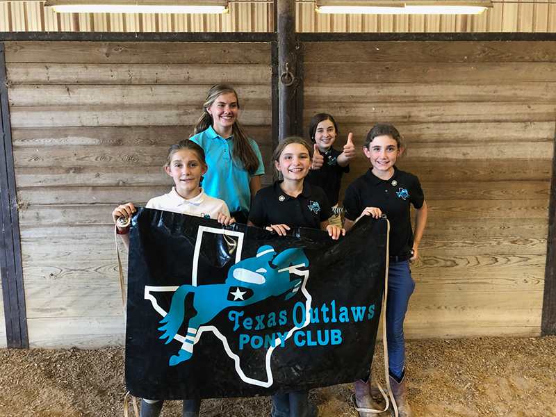 A group of young girls holding a banner with the name of their Pony Club on it.