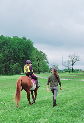 A young girl riding her horse with someone walking beside her.