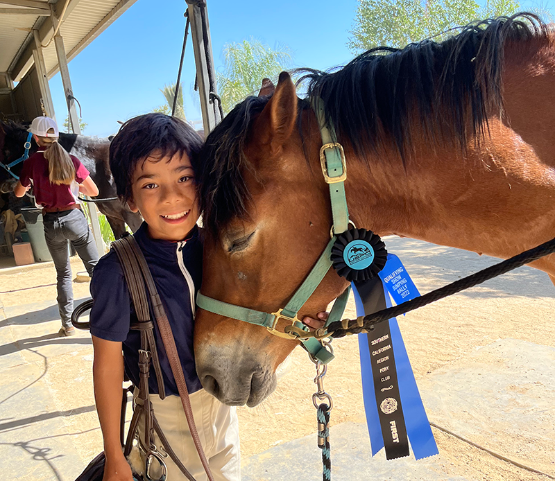 A young boy with his horse, smiling at the camera.