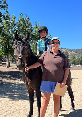 A young boy on his horse, smiling at the camera with an instructor.