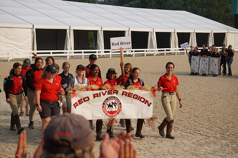 A group of young adults walking with a sign for their Pony Club Region.