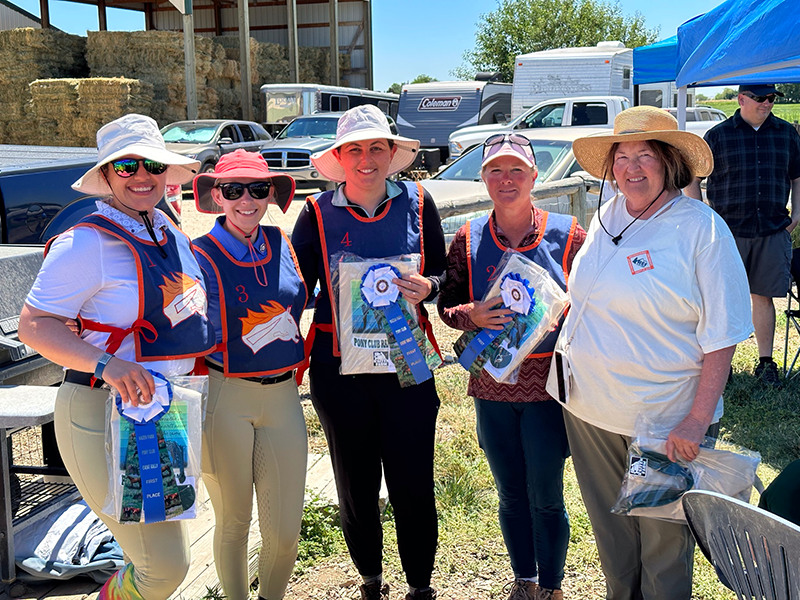 A group of adults standing in front of the camera, smiling as they hold first place ribbons.