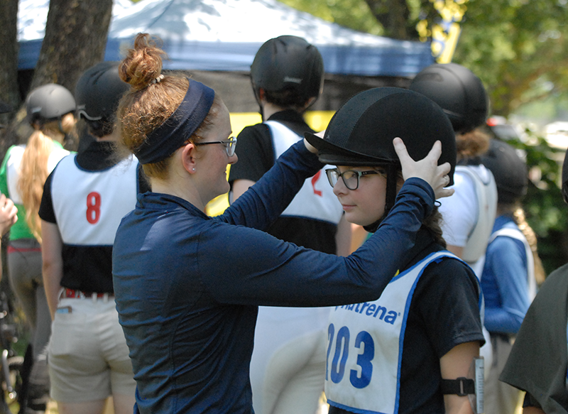 A young woman checking the fit of a helmet on a young rider.