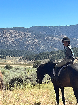 A young boy on his horse, on top of a mountain. The boy is turned over his shoulder, smiling to the camera.