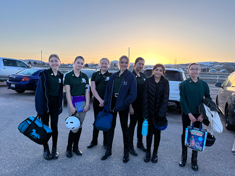 A group of young looking women in a parking lot, smiling at the camera as the sun rises behind them.