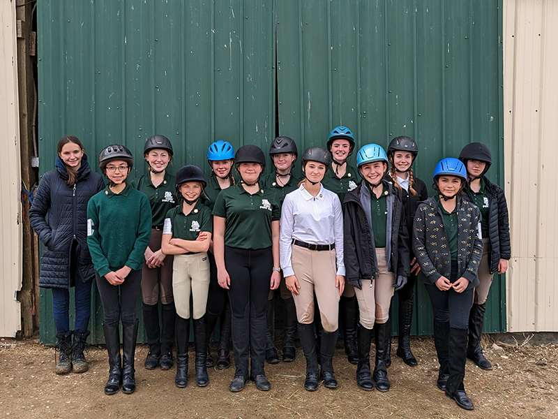 A group of young horse riders, standing in front of the camera, smiling.