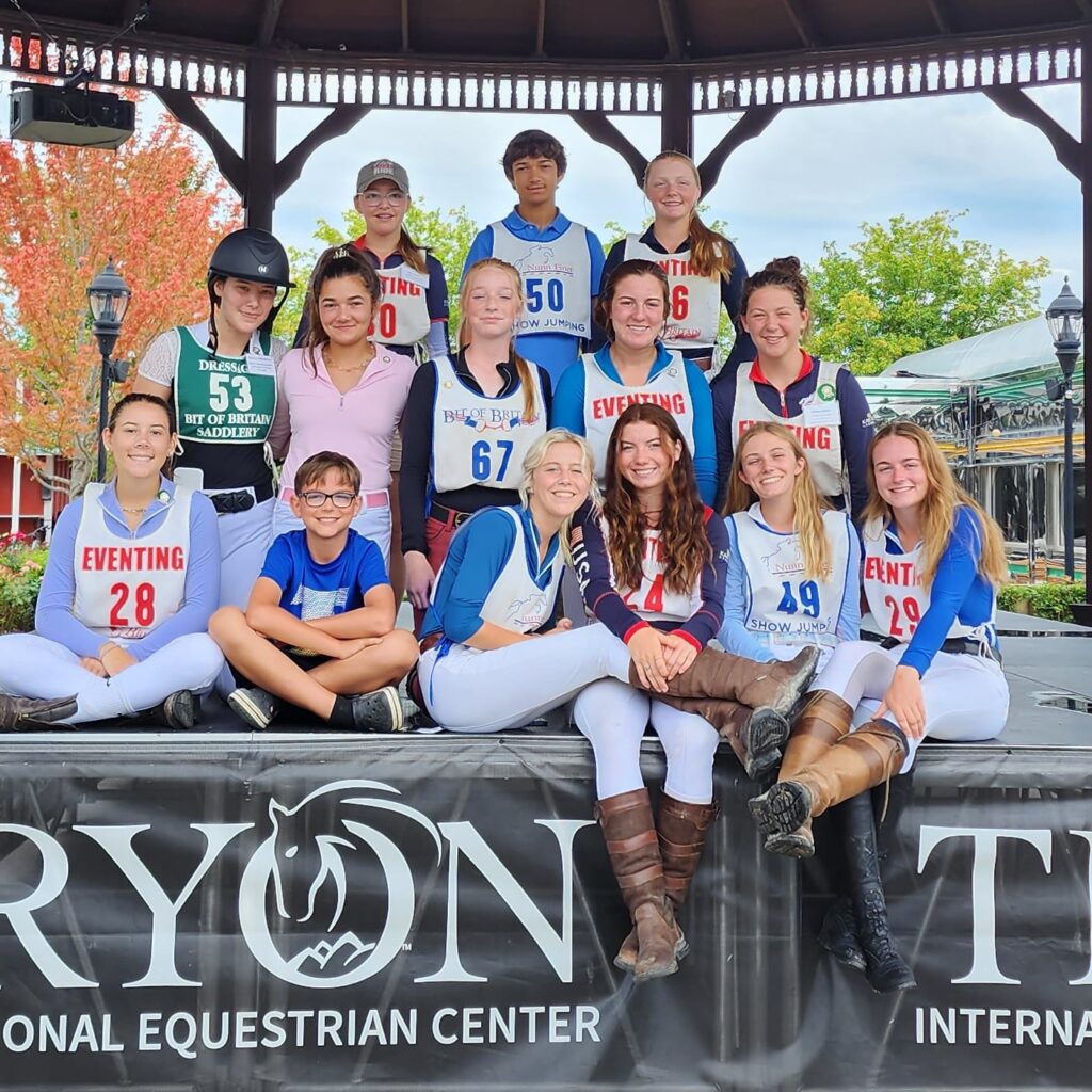 A group of young kids dressed in horse riding clothes, standing together for a group picture.