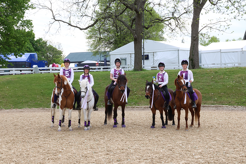 A ground of individuals on their horses, standing and smiling at the camera.