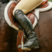 A person riding a horse, the image is zoomed in to just the saddle and the left leg of the rider.