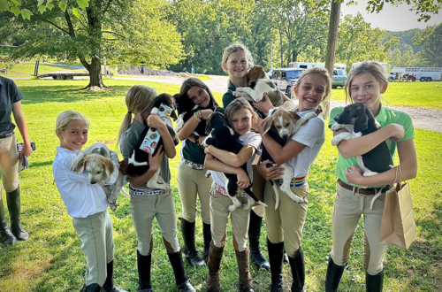 A group of young kids holding puppies, smiling at the camera with the Elkridge-Harford Pony Club