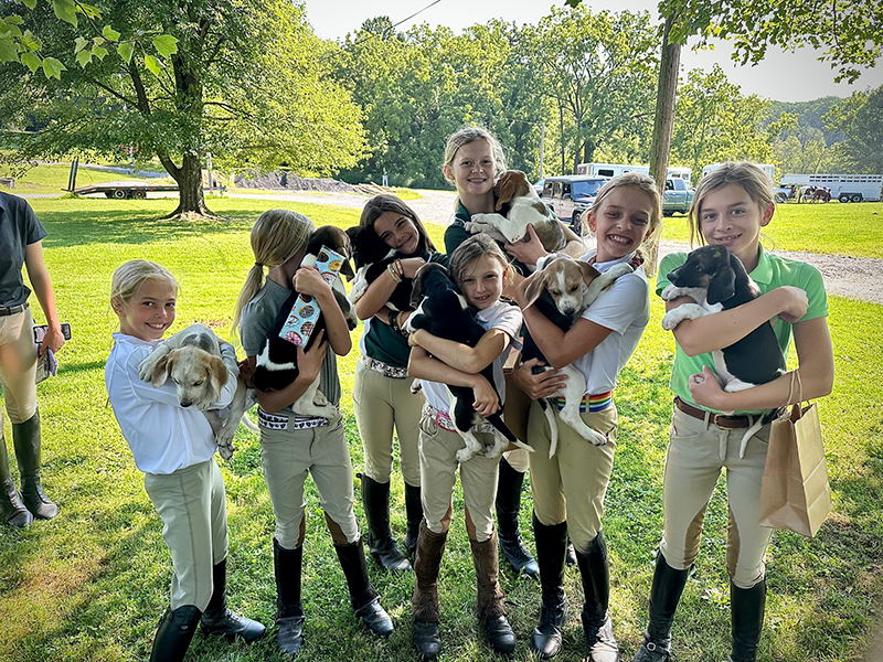 A group of young kids holding puppies, smiling at the camera with the Elkridge-Harford Pony Club