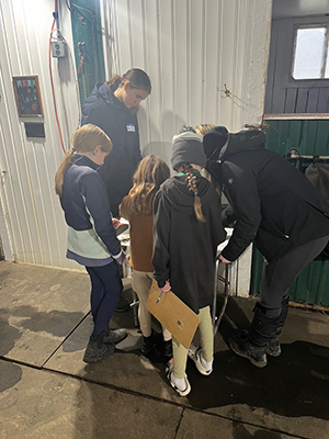 A young woman teaching a group of young children in a barn.