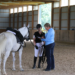 An examiner explaining something to a student who is holding their horse on the lunge line.