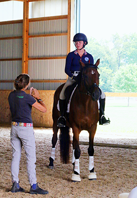 An examiner explaining something to a student who is riding a horse.