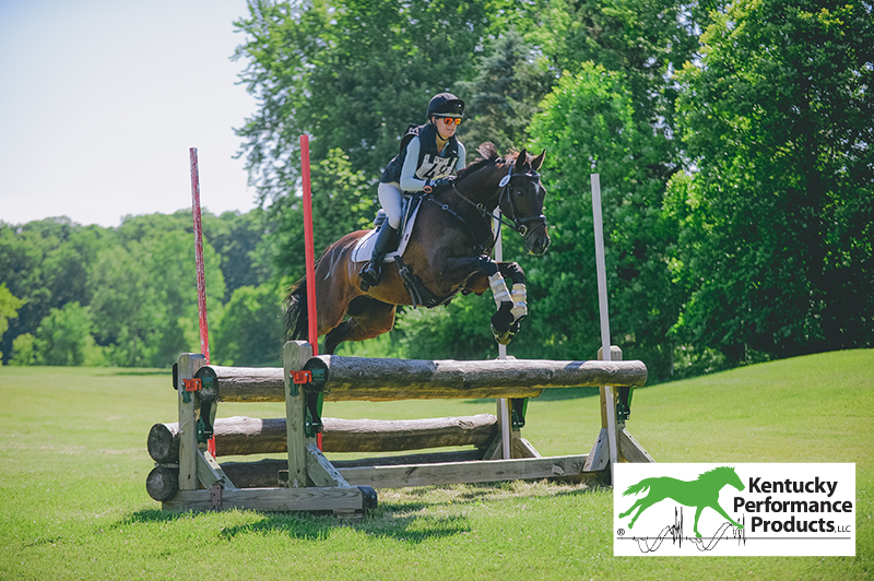 A young woman jumping her horse over a cross-country fence.
