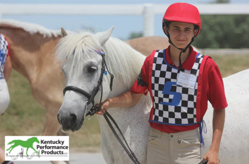 A young man walking his horse, smiling at the camera.