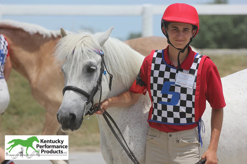 A young man walking his horse, smiling at the camera.