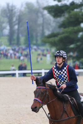 A young man riding his horse, carrying a pole.