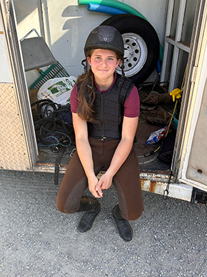 A young girl sitting in a horse trailer, smiling at the camera.