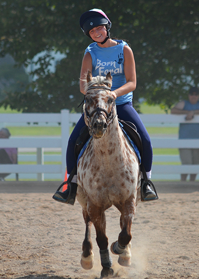A young girl riding her pony, smiling.