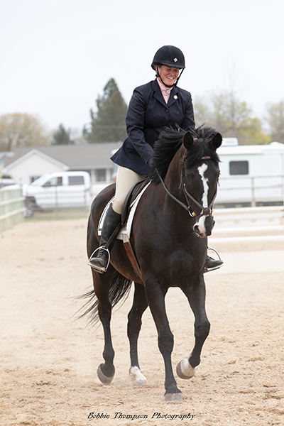A woman riding a horse in an arena, smiling.