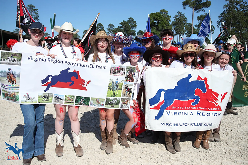 A group of young riders holding banners, smiling for the camera.