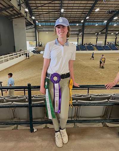 A young woman posing in an arena with awards.