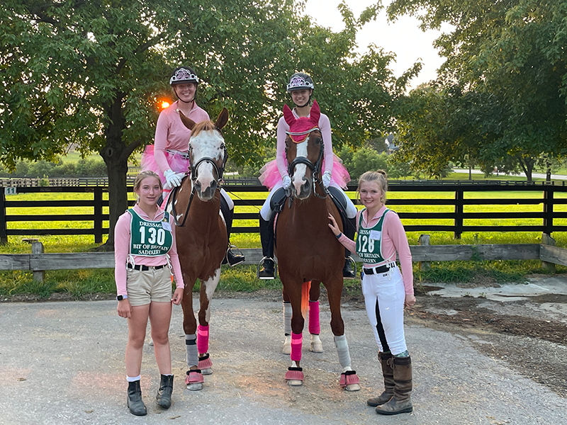 A group of young women smiling for the camera, two of the women and on horseback.