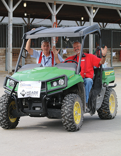 Two men in a golf car, waving at the camera.
