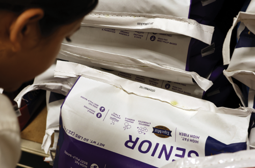 A woman looking closely at the bottom of a bag of horse feed.