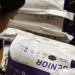 A woman looking closely at the bottom of a bag of horse feed.