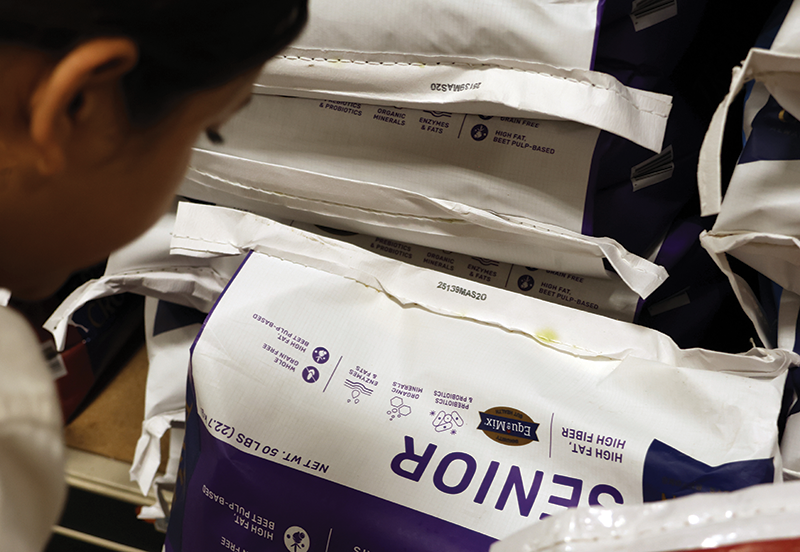 A woman looking closely at the bottom of a bag of horse feed.