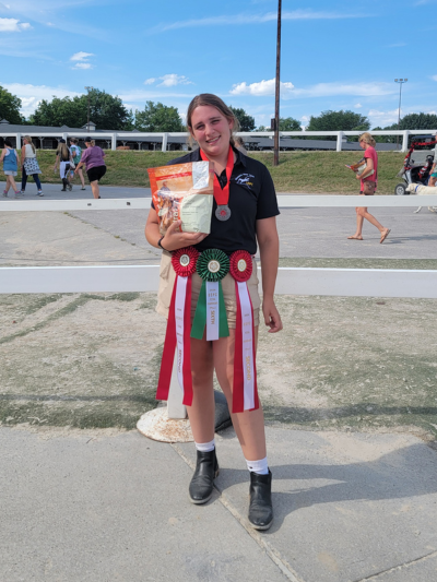 A young woman with ribbons around her belt, smiling at the camera and holding a bag of salt for horses.