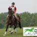A young woman riding a horse on a cross-country course, smiling.